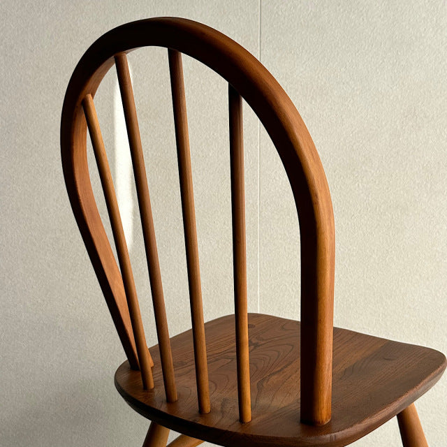 Vintage British mid-century ERCOL hoop back dining chair in warm teak with curved spindle back and visible wood grain.