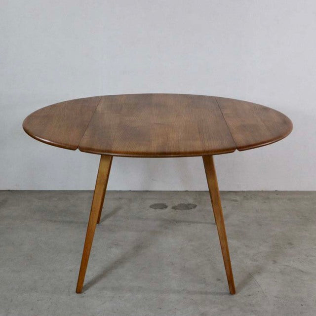 Mid-century British vintage Ercol dining table in teak with drop-leaf oval top and slender tapered legs showcasing rich wood .