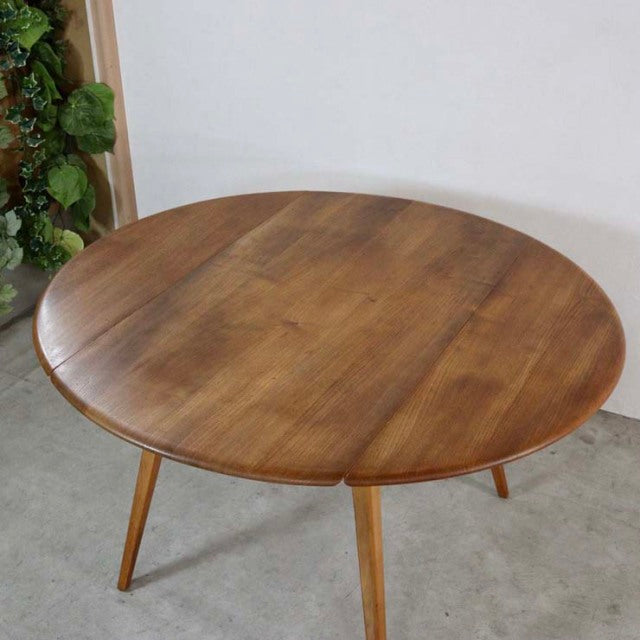 Vintage British mid-century Ercol teak dining table with drop-leaf, round top, and tapered legs.