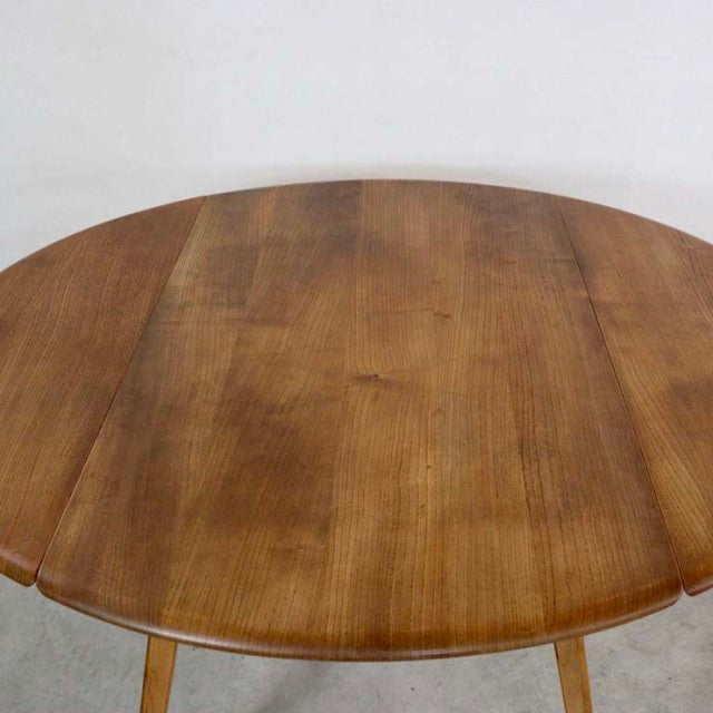 Round vintage teak dining table with drop-leaf design, smooth wood grain, mid-century British style with slender tapered legs.