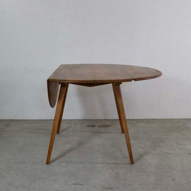 Mid-century British vintage Ercol teak dining table with drop-leaf, smooth oval top, and angled tapered legs.