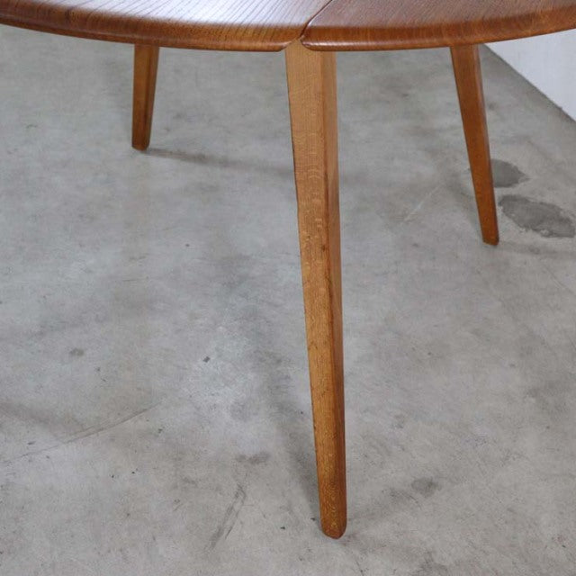 Mid-century British vintage Ercol dining table in teak with smooth oval top and tapered round legs showing rich wood grain.