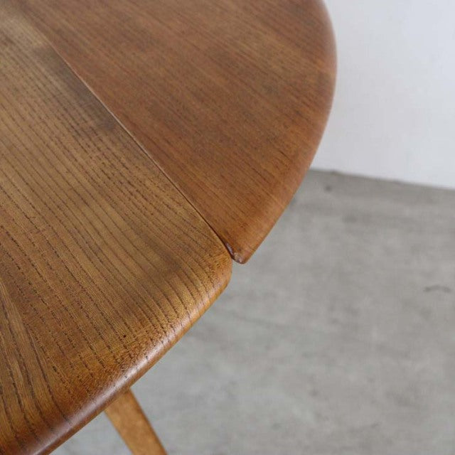 Close-up of vintage British mid-century Ercol teak drop-leaf dining table corner showing smooth wood grain and rounded edges.