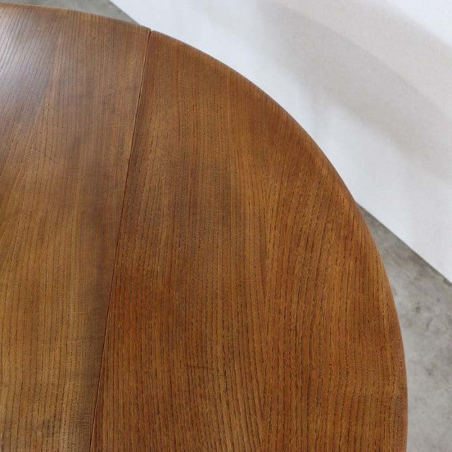 Round vintage British mid-century dining table in teak with smooth wood grain and drop-leaf design.