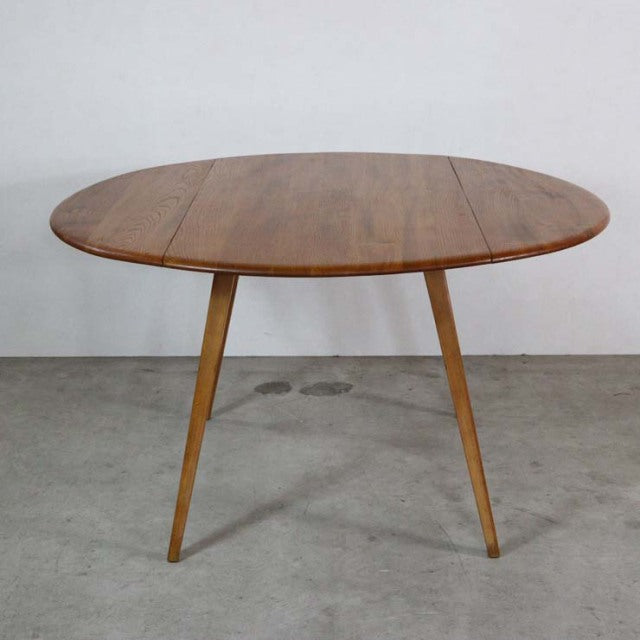 Vintage British mid-century Ercol dining table in teak with round drop-leaf top and slender tapered legs.
