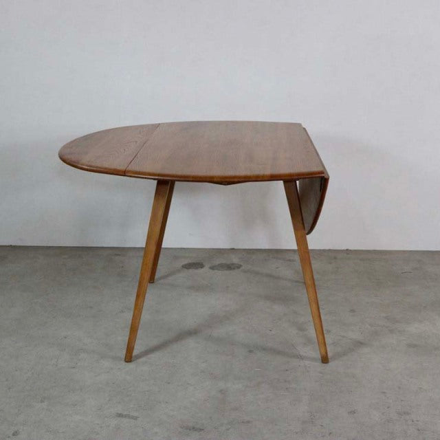 Mid-century British vintage Ercol dining table in teak with drop-leaf design and slender angled legs showing rich wood grain.