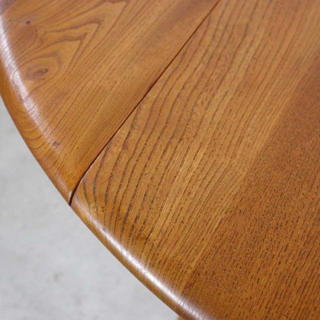 Close-up of vintage mid-century British Ercol dining table corner, warm teak wood grain, gently curved edge.