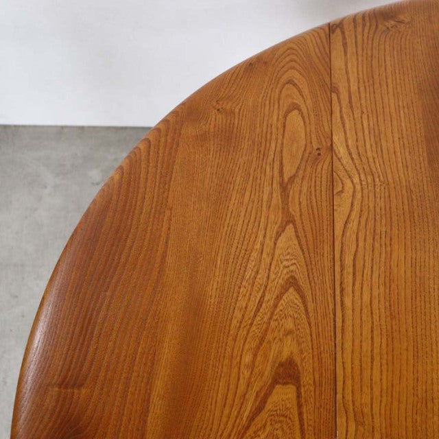 Mid-century British Ercol teak dining table with drop-leaf, smooth rounded edge, visible wood grain, slender tapered legs.
