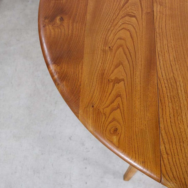 Vintage mid-century British Ercol dining table in warm teak with smooth rounded drop-leaf edge and visible wood grain on.