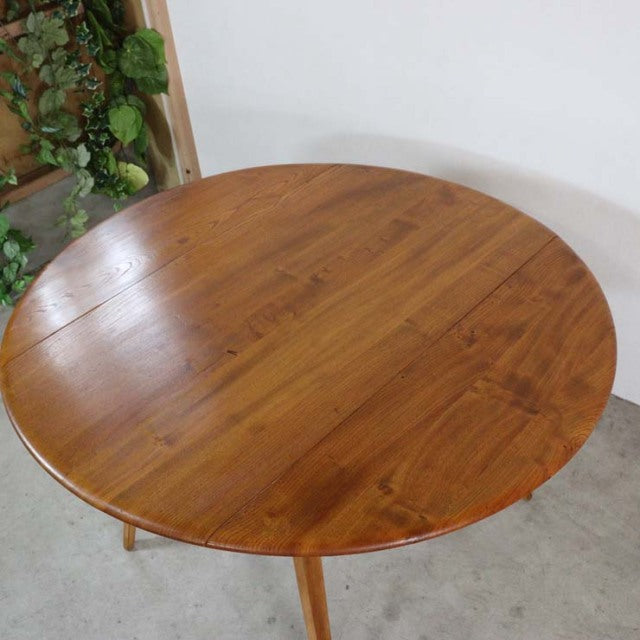Round vintage teak dining table with visible wood grain and slender mid-century British legs.