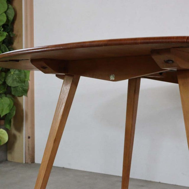 Mid-century British Ercol dining table in warm teak with rounded drop-leaf top and angled slender legs showcasing natural.