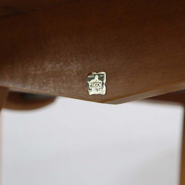 Close-up of a vintage British Ercol dining table's teak wood edge showing smooth grain and branded metal label, mid-century.