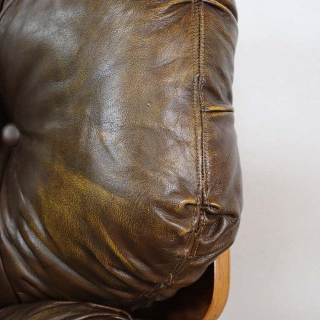 Close-up of vintage mid-century British leather armchair showing rich brown leather with natural creases and stitched seams, .