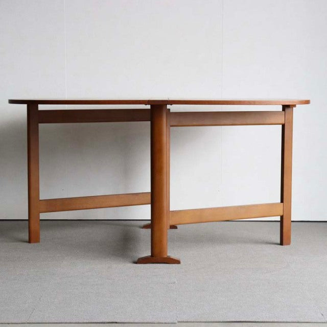 Vintage mid-century teak dining table with folding top and sturdy British-Denmark style legs showcasing rich wood grain.