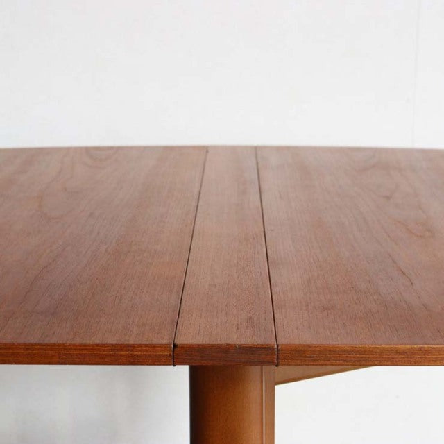 Mid-century British teak dining table with folding leaf, visible wood grain, and rounded legs.