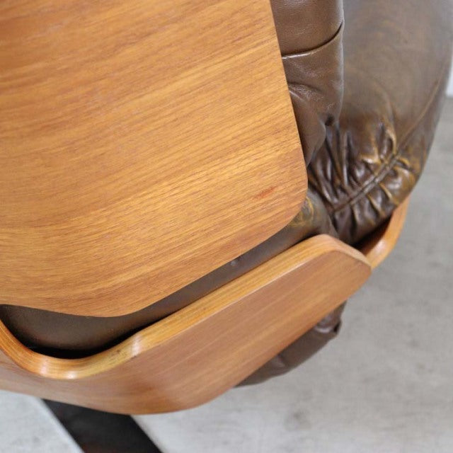 Close-up of vintage mid-century British teak armrest with smooth wood grain and dark brown leather upholstery.