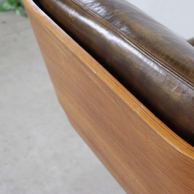 Mid-century British vintage leather armchair with curved teak wood frame and natural grain visible.
