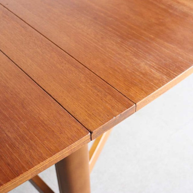 Vintage mid-century British teak dining table with smooth wood grain and folding mechanism visible on rounded edge.