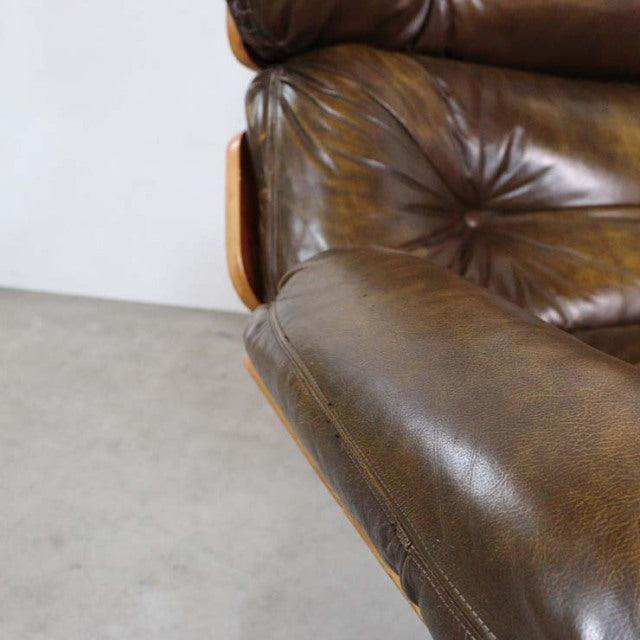 Vintage mid-century British sofa featuring rich brown leather upholstery and smooth teak wood armrests with visible grain.