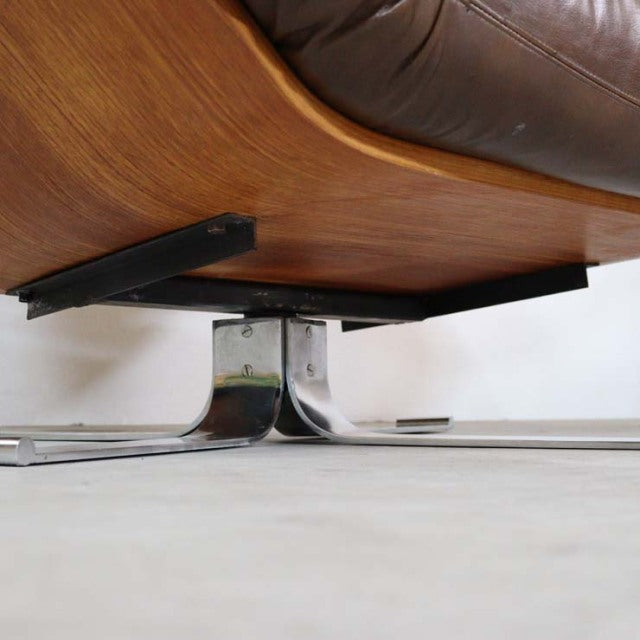 Close-up of vintage teak base with chrome swivel legs supporting mid-century British leather armchair from Denmark.
