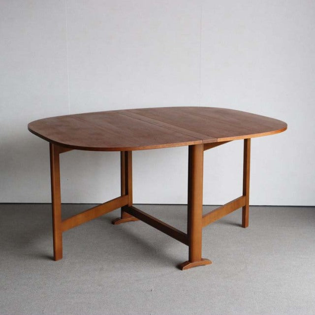 Vintage mid-century teak dining table with rounded edges and folding leaf, British-Denmark style, showcasing smooth wood.