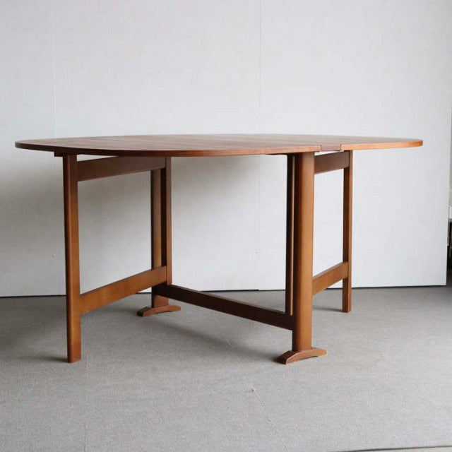 Vintage mid-century British teak dining table with folding oval top, showcasing warm wood grain and sturdy angled legs in.