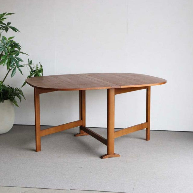 Vintage mid-century teak dining table with rounded top, folding design, and sturdy British-Denmark style legs.