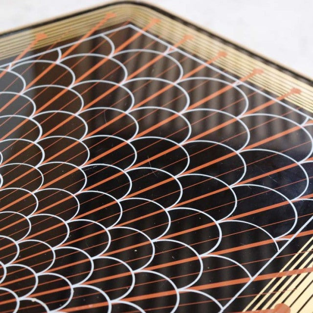 Close-up of vintage teak mid-century coffee table top with black lacquer and intricate white and orange geometric pattern,.