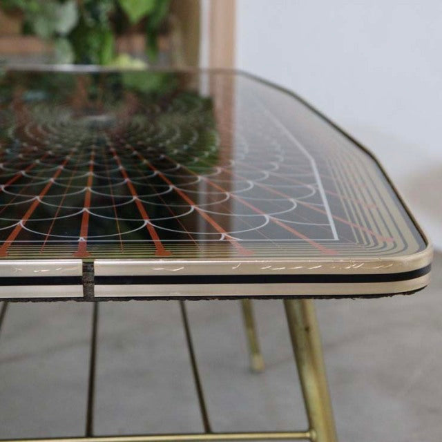 Mid-century vintage British teak coffee table with glass top featuring geometric pattern and slender brass legs.