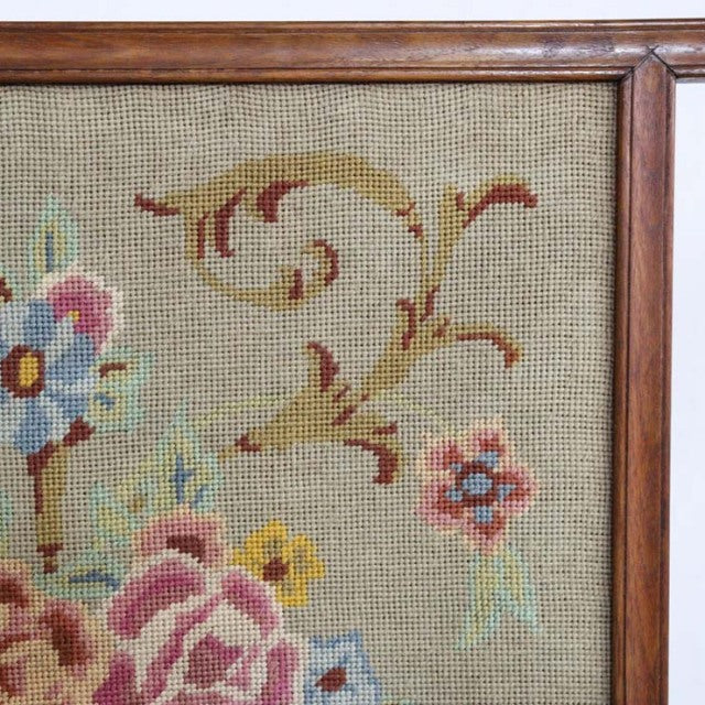 Close-up of vintage teak mid-century British fire screen corner with floral needlepoint embroidery and wood grain frame.