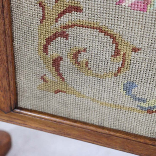 Close-up of vintage British mid-century teak fire screen corner with woven tapestry fabric featuring floral scroll details.