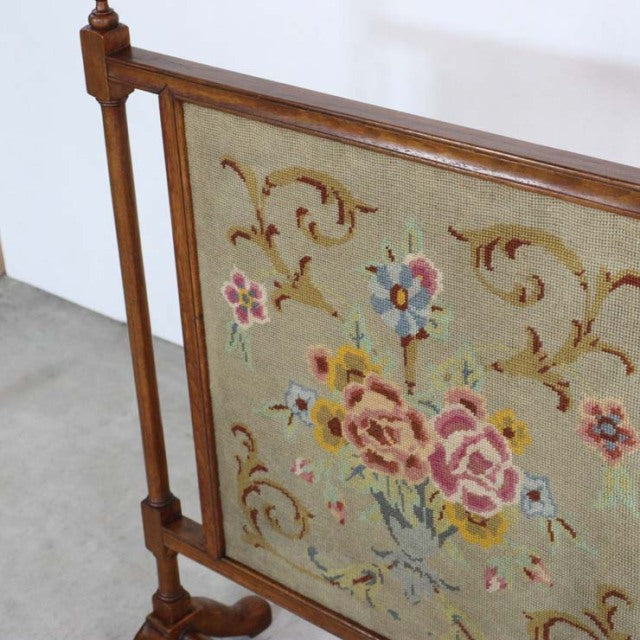Mid-century vintage British fire screen with teak frame and floral tapestry panel featuring pink, blue, and yellow flowers.
