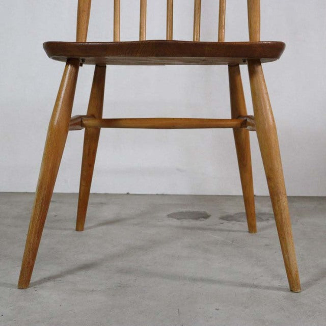 Vintage mid-century British Ercol Quaker chair with teak seat, angled light wood legs, and visible wood grain.
