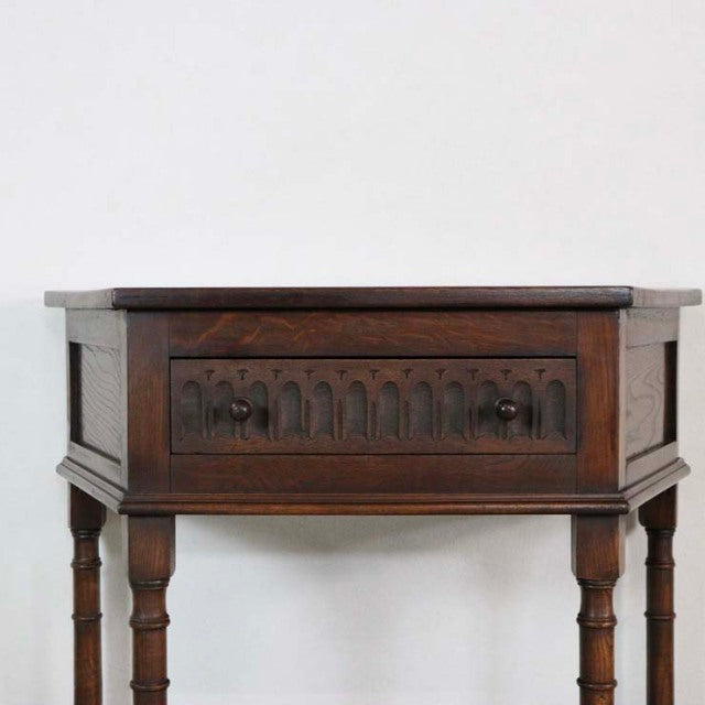 Vintage British mid-century teak bedside cabinet with carved drawer front and turned legs in rich dark wood finish.