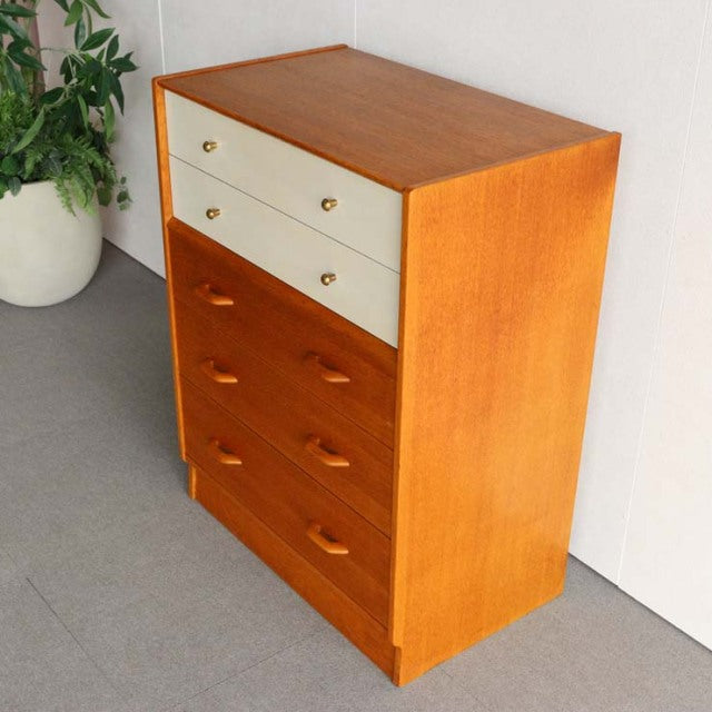 Mid-century British G-PLAN chest in teak with Chinese white top drawers, brass knobs, classic wood grain, and tapered legs.