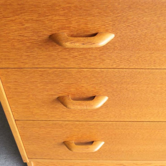Mid-century British G-Plan teak chest with three drawers, smooth wood grain, sleek recessed handles, and tapered legs.