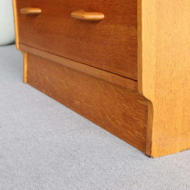 Mid-century British vintage teak chest with smooth grain, rounded handles, and light oak frame legs.