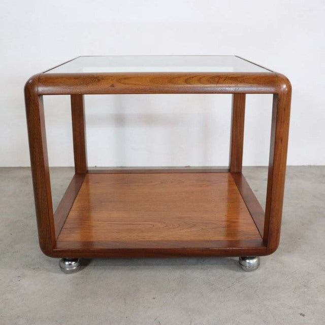 Vintage British mid-century teak cube coffee table with glass top and rounded edges on caster wheels.