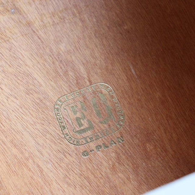 Close-up of vintage G-Plan teak wood grain with mid-century British furniture gold stamp emblem.