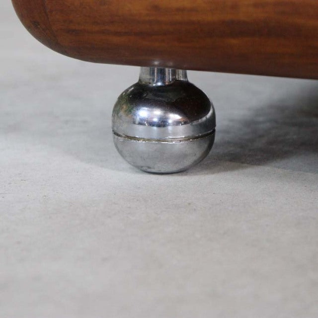 Close-up of a polished chrome spherical leg supporting a vintage British mid-century teak coffee table with smooth wood.