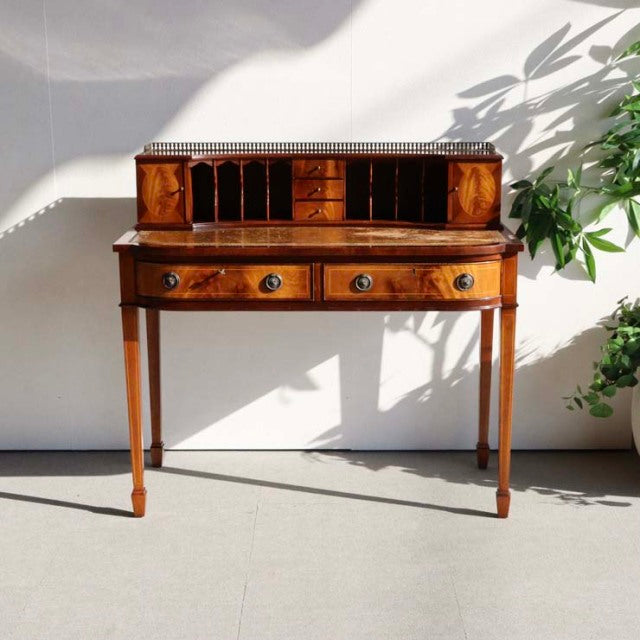 Mid-century British vintage teak desk with rich wood grain, three drawers, and slender tapered legs.