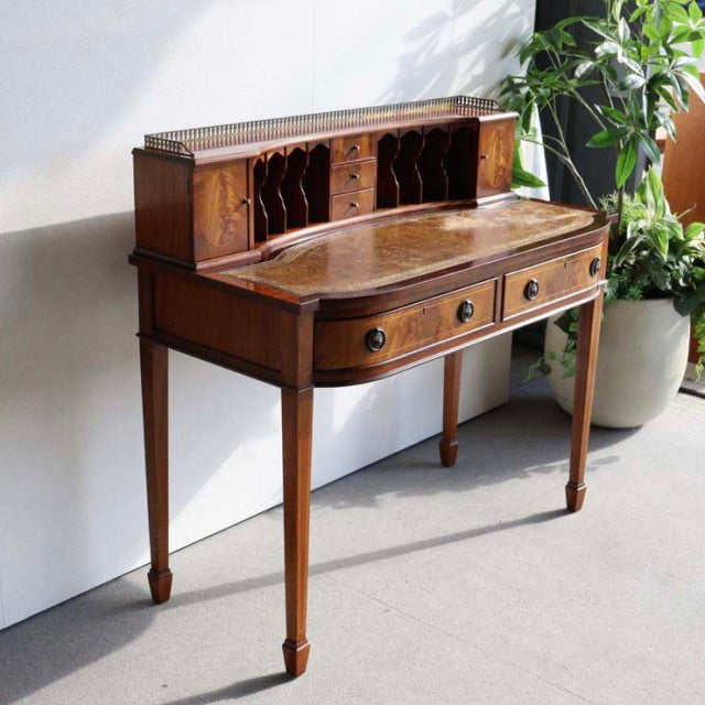 Vintage mid-century British teak desk with curved top, carved wood grain, tapered legs, and upper pigeonhole compartments.