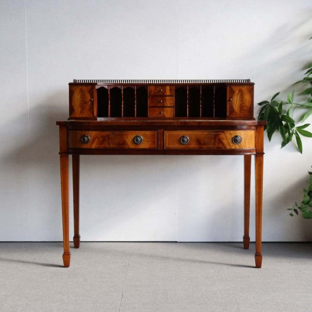 Vintage British teak mid-century desk with polished wood grain, slender tapered legs, and raised back organizer drawers.