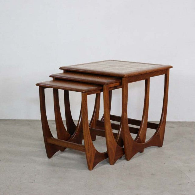 Set of three vintage G-Plan teak nest tables with mid-century British design, curved legs, and visible wood grain.