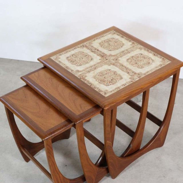Set of three vintage teak G-plan nest tables with British mid-century design, featuring decorative tile top on largest table .