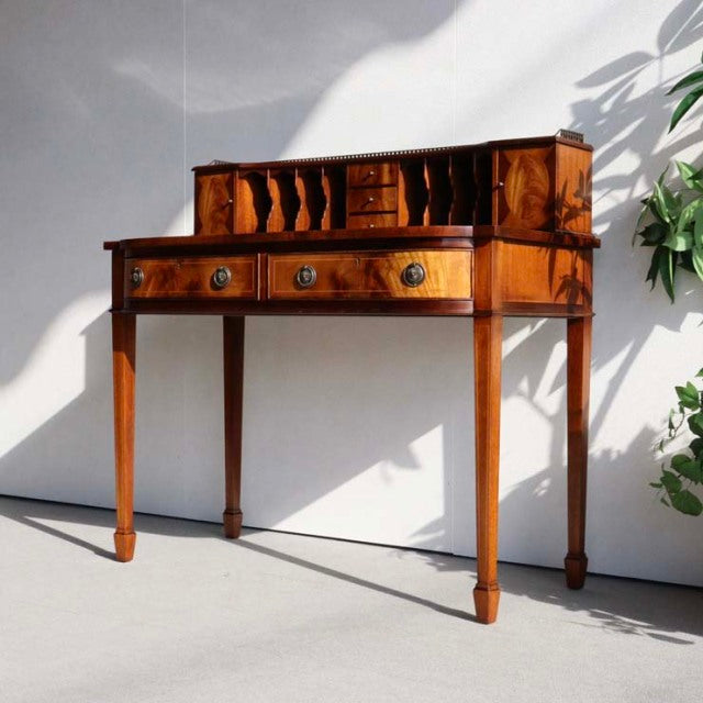 Vintage British mid-century teak desk with elegant wood grain, slender tapered legs, and small upper drawers from Denmark.