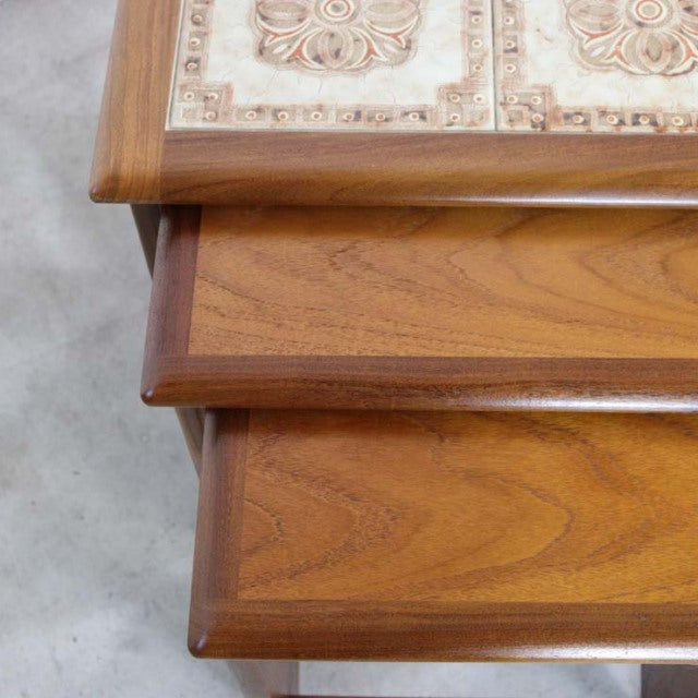 Stacked vintage British teak G-plan mid-century nest tables with visible wood grain and tile insets.