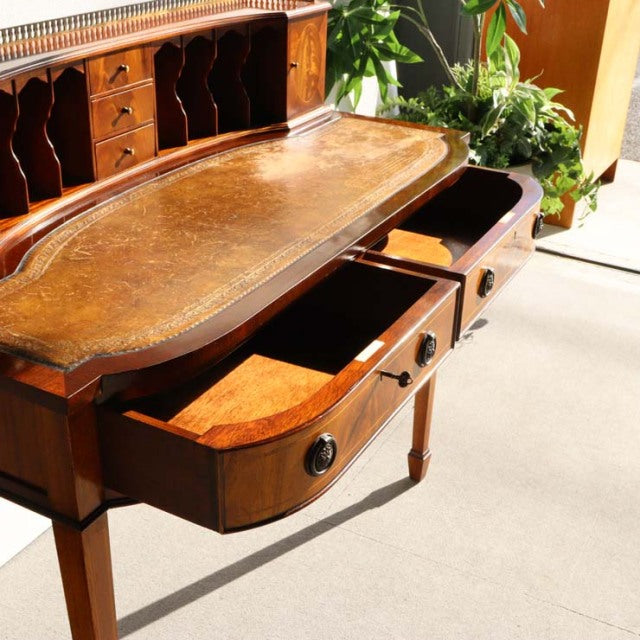 Vintage British mid-century teak desk with intricate wood grain, curved drawer fronts, and slender tapered legs, styled in.