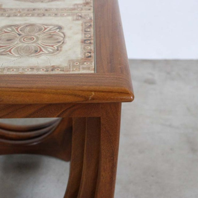 Vintage teak G-Plan British mid-century nest table corner with decorative tile top and curved wood legs.