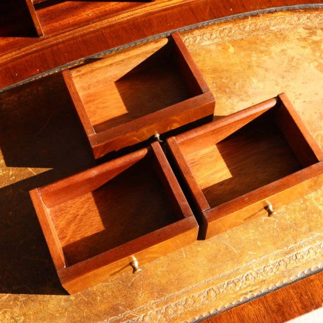 Three vintage teak drawers with rich wood grain and brass knobs, set on a British mid-century desk surface with ornate.